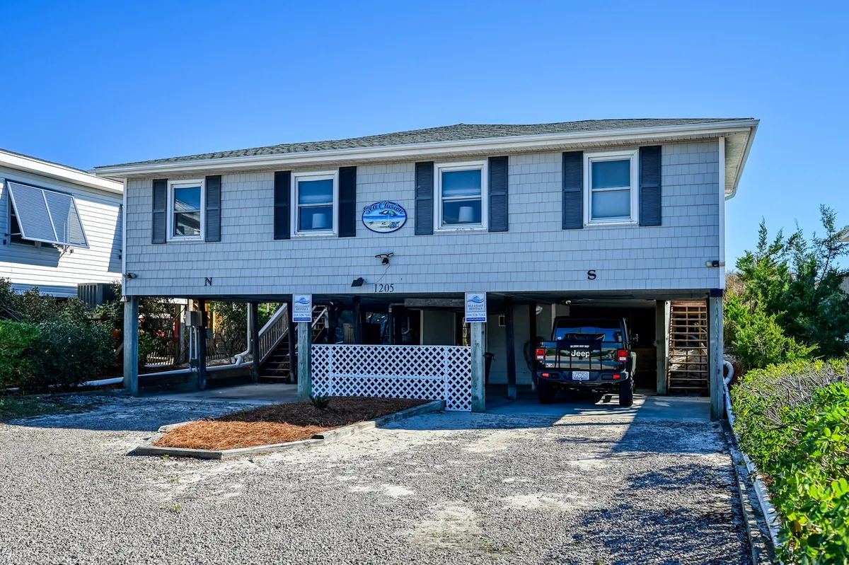 An exterior view of the house facade, featuring a sign above the door and a vehicle parked outside. The welcoming porch and visible entryway highlight the home's accessible entry features and outdoor friendliness.