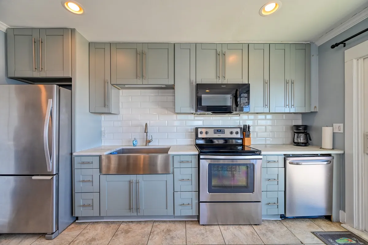 A modern kitchen is featured with stainless steel appliances, a deep farmhouse sink, sleek cabinetry, and an artistic tile backsplash. The clean, inviting space is set up for cooking and entertaining, with natural light and a contemporary feel throughout.