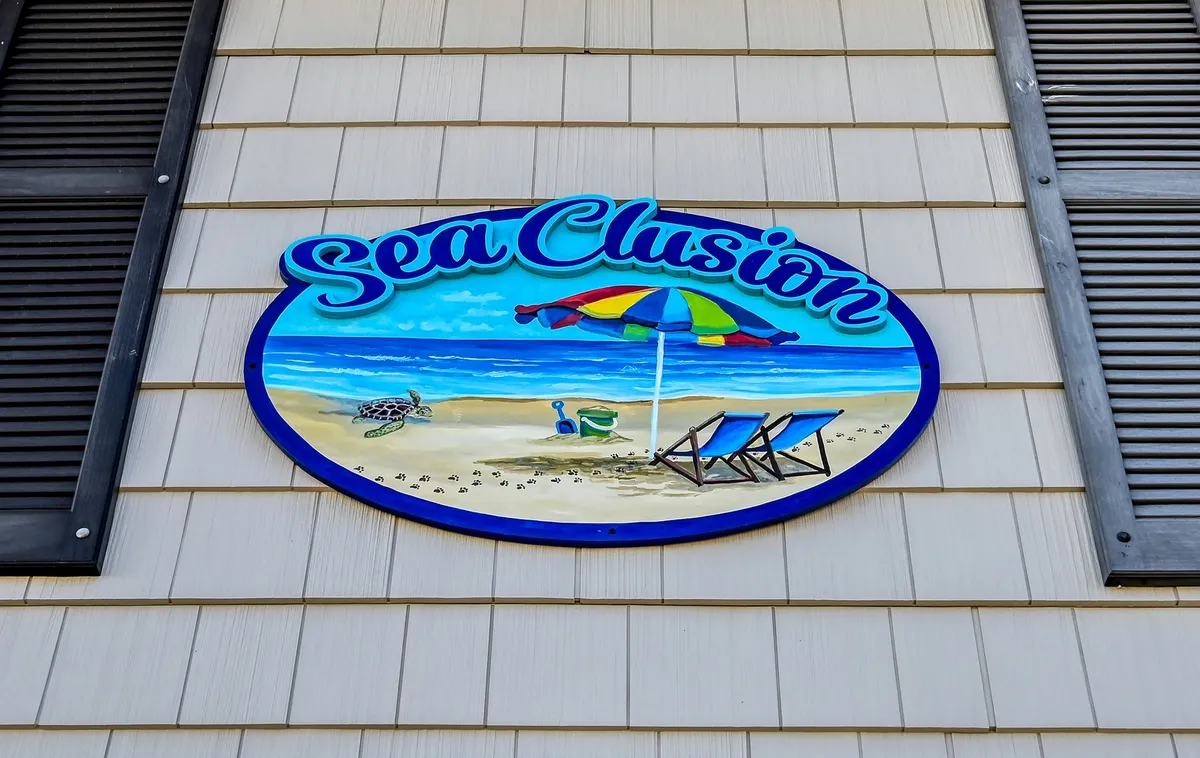 A cheerful exterior scene with a colorful beach-themed sign, umbrella, and lounge chairs set up for fun and relaxation. The vibrant setting reflects the playful, family- and pet-friendly atmosphere of the area, hinting at all the local adventures awaiting beyond the house.