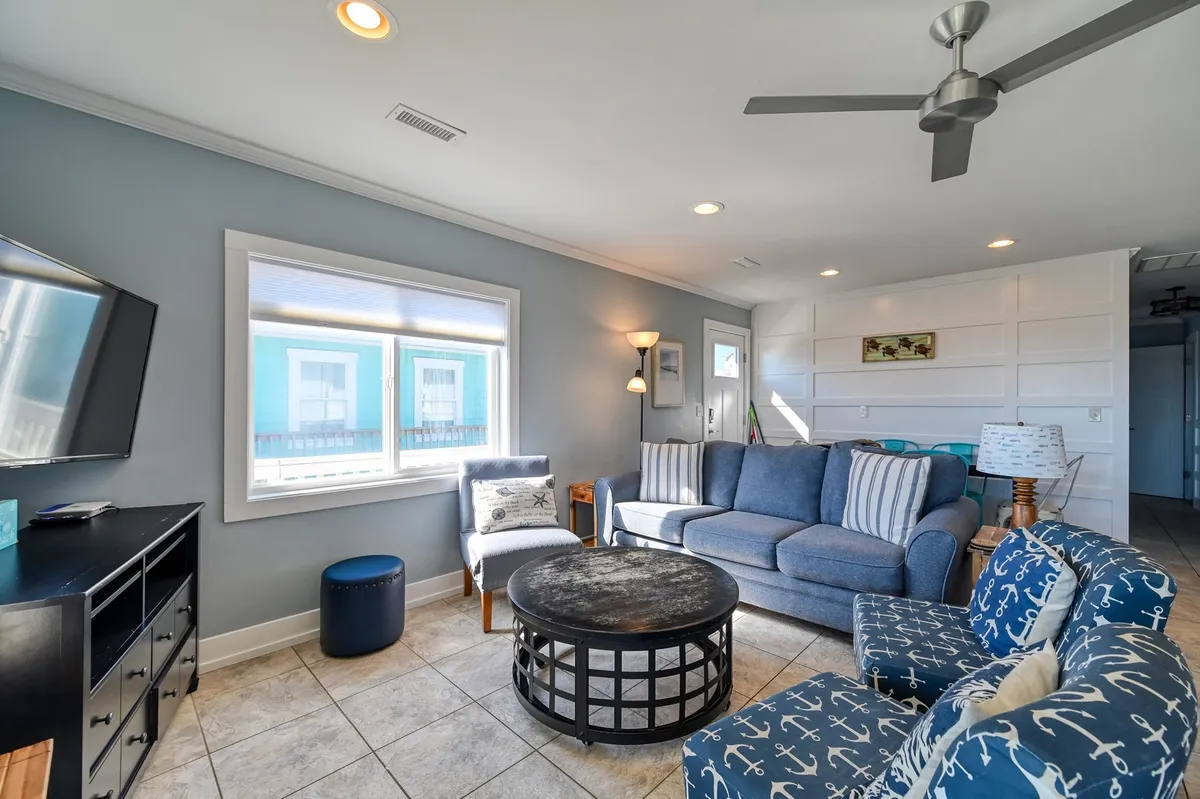A bright, inviting living space with a blue sofa, anchor-patterned chairs, and a coffee table, arranged for socializing and relaxation. The decor subtly nods to nautical themes, reinforcing the coastal location and the idea of gathering to share experiences after a day of exploring.