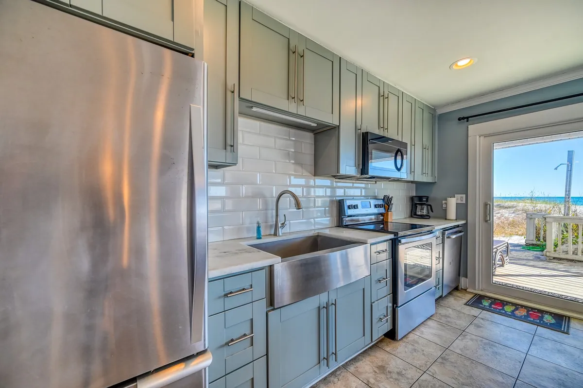 A view of a modern kitchen with stainless steel appliances, a large sink, an inviting kitchen island, and a sliding glass door that hints at access to outdoor spaces. The room is bathed in natural light, creating a welcoming connection between interior comfort and the exterior environment.