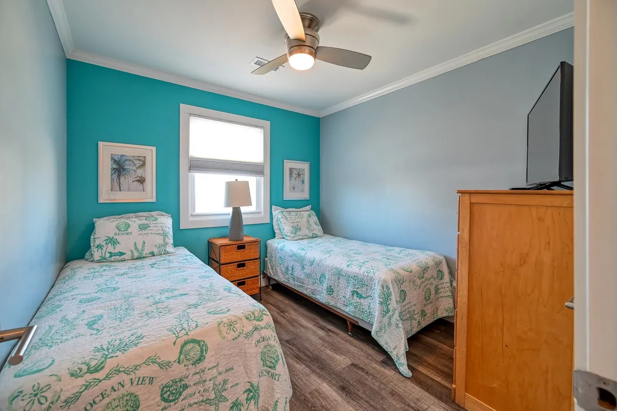 An inviting twin bedroom with two twin beds, colorful wall art, a lamp, and a dresser. The cheerful decor and cozy layout are perfect for families or groups sharing the space.
